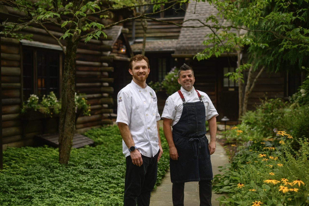 The two chefs at Glendorn stand outside the entrance with the trees and greenery.
