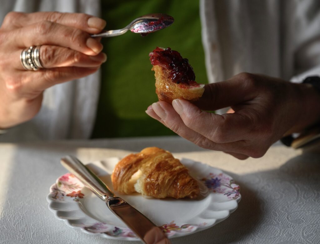 A person slathers Glendorn blackberry jam on a croissant.