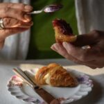 A person slathers Glendorn blackberry jam on a croissant.