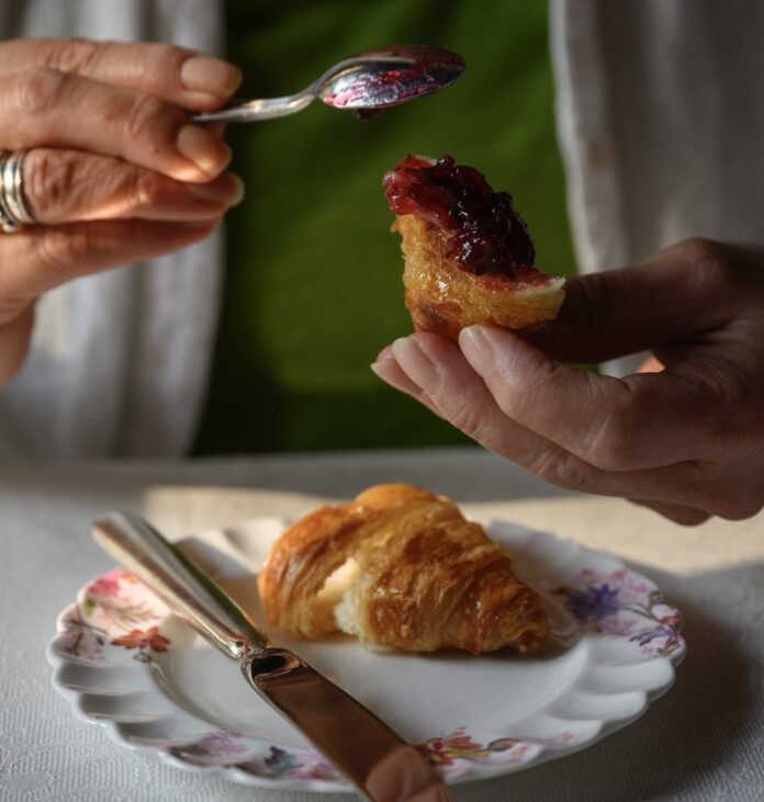 A person slathers Glendorn blackberry jam on a croissant.