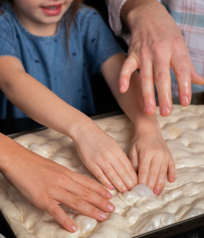 Two sets of hands knead a sourdough pizza dough on a black table.