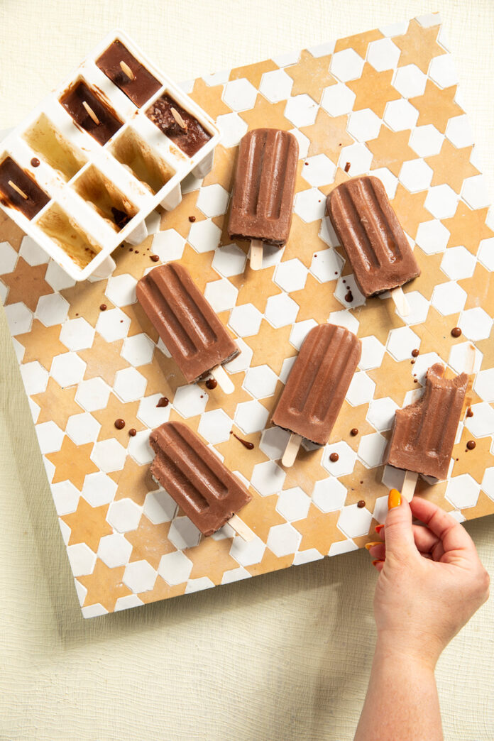 Six boozy fudgesicles on a white and yellow tiled background, with more in popsicle molds