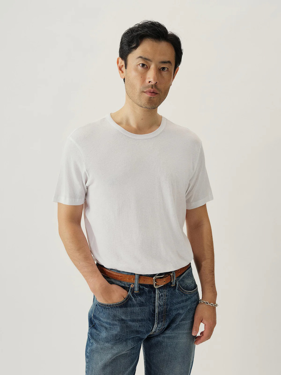A man in a white t-shirt on a white background with jeans and a brown belt on