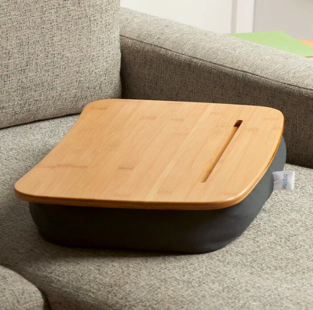 A lap desk, tan wood on a black cushion, on a beige chair, ready to be used by a new college student