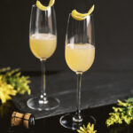 An earl grey cocktail, but yellow in color, on a black background staged with flowers