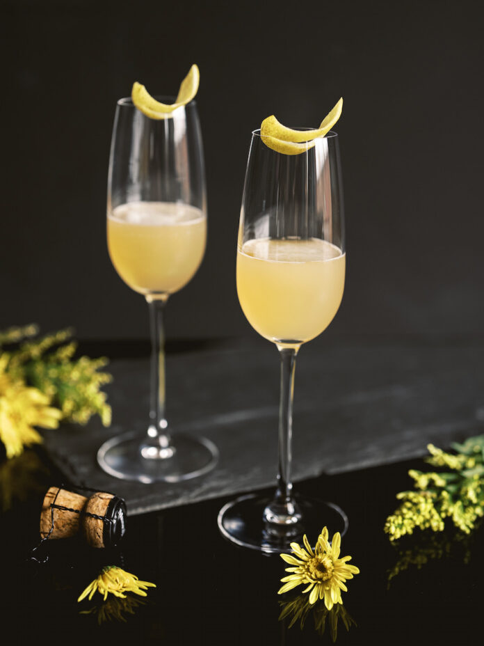An earl grey cocktail, but yellow in color, on a black background staged with flowers