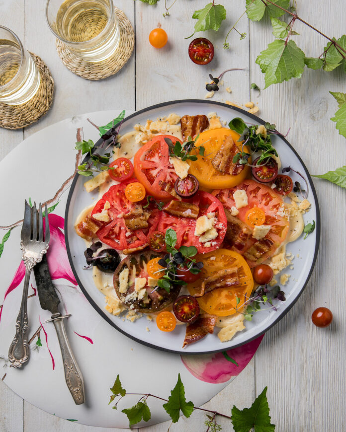 A plated BLT salad with large red heirloom tomatoes in it on a white background
