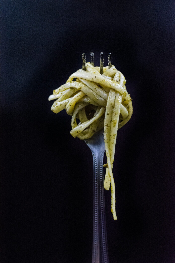 A fork with pasta, an recipe, swirled around it on a black background
