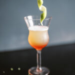 A gradient of orange and red cocktail with a spiral on top on a black background