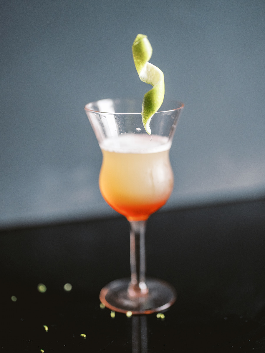 A gradient of orange and red cocktail with a spiral on top on a black background