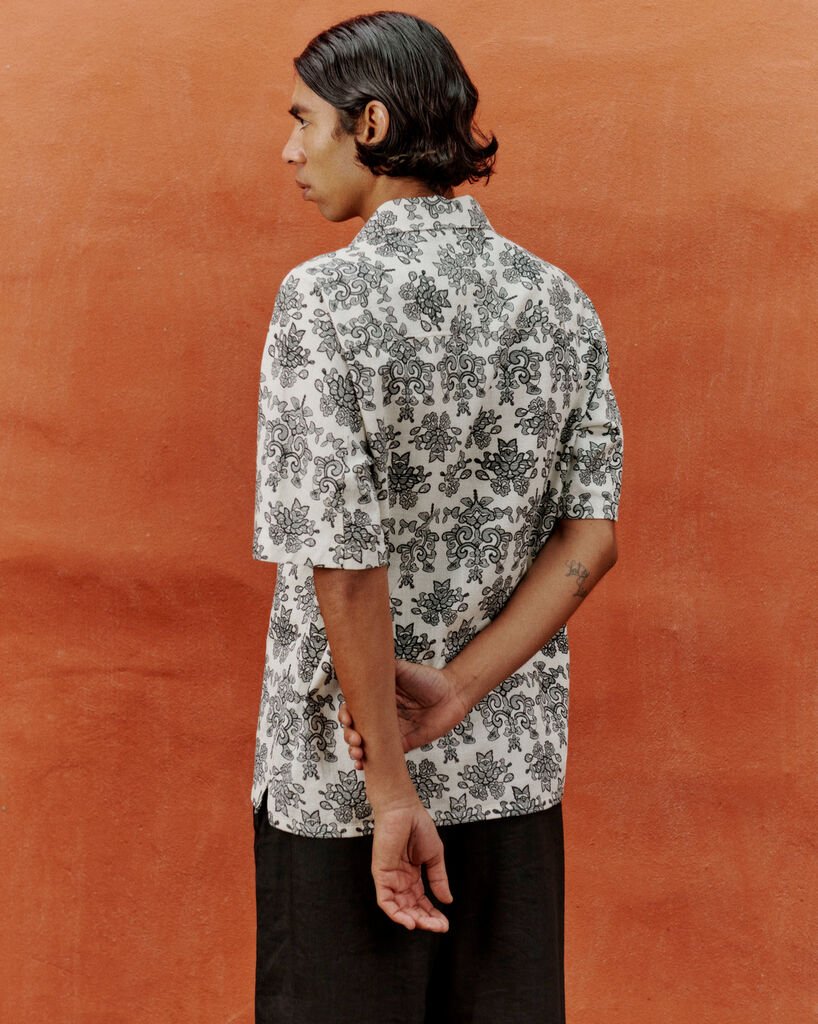 A man with a patterned shirt on an orange background, in a summer outfit