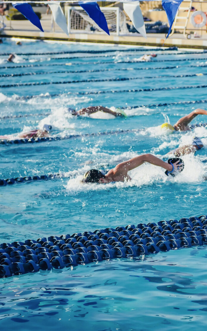 An Olympic swimmer in a bright blue pool with dark blue and white flags above it