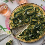 A zucchini tart on a white background, garnished with flowers