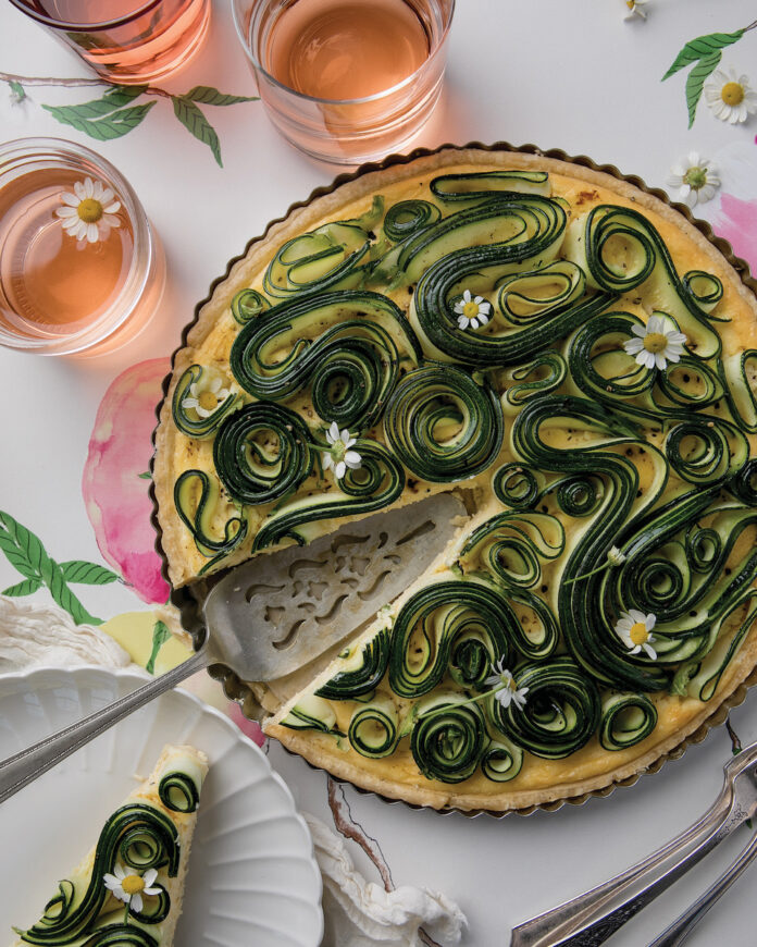 A zucchini tart on a white background, garnished with flowers