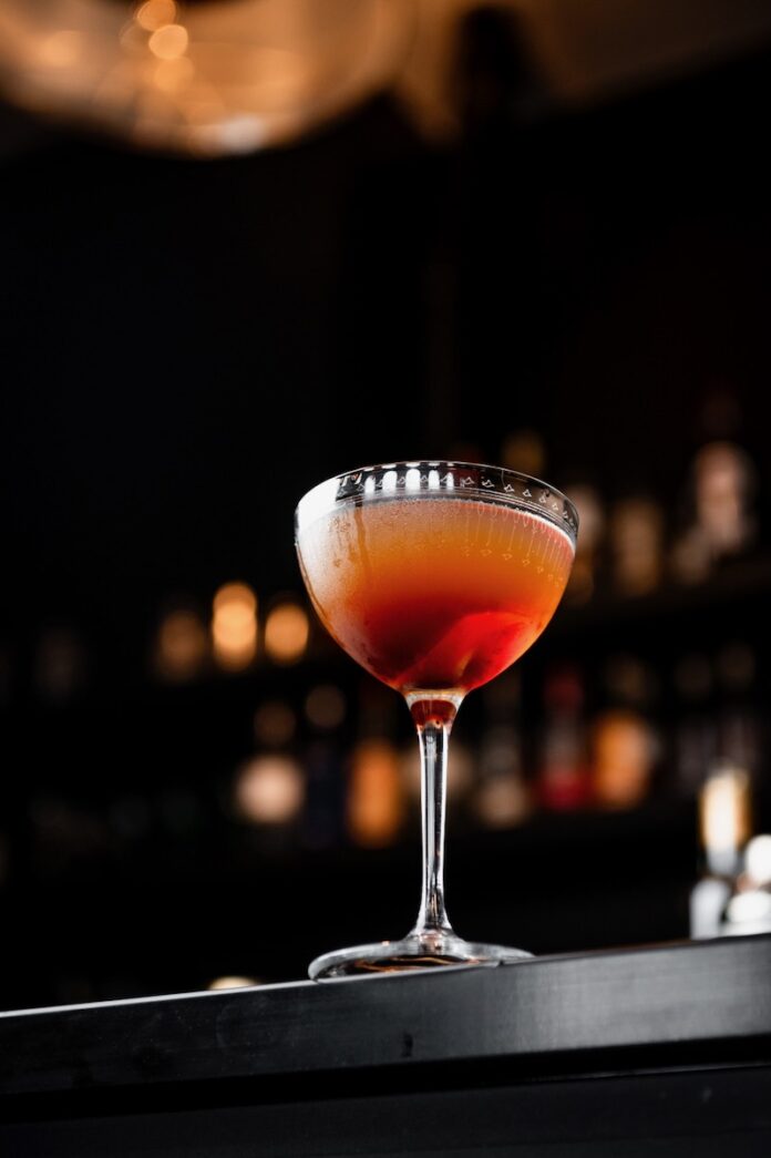 A tall glass sits on a bar with an orange and red hue to represent the Bene Gesserit in Dune Prophecy.