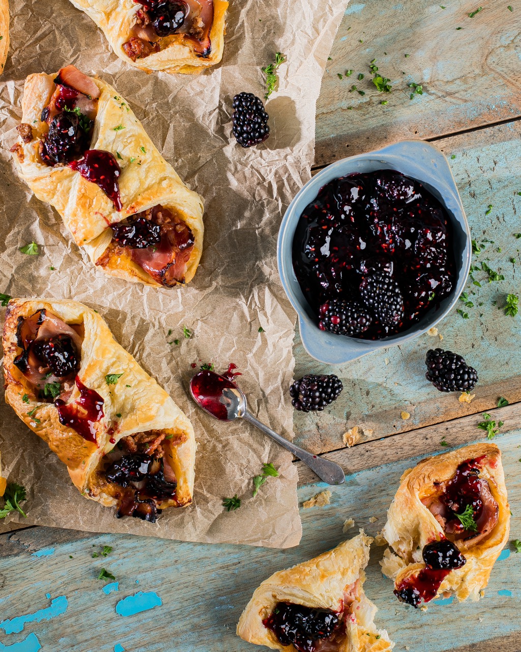 Three Breakfast pastry puffs sit on butchers paper beside a small bowl of blackberry topping.