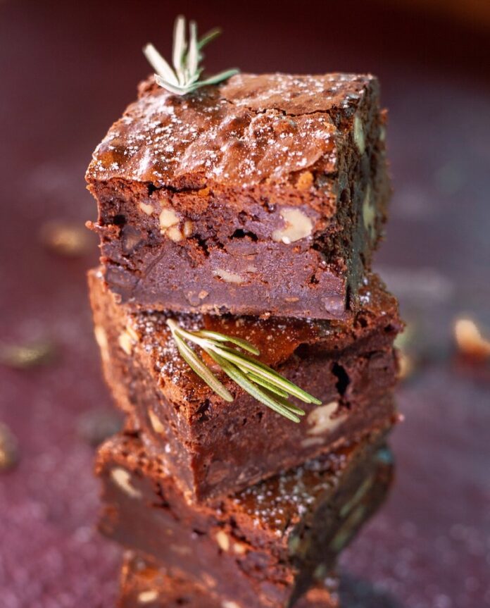 Four brownies with nuts in the center stack on top of each other with a fudge ganache on top.