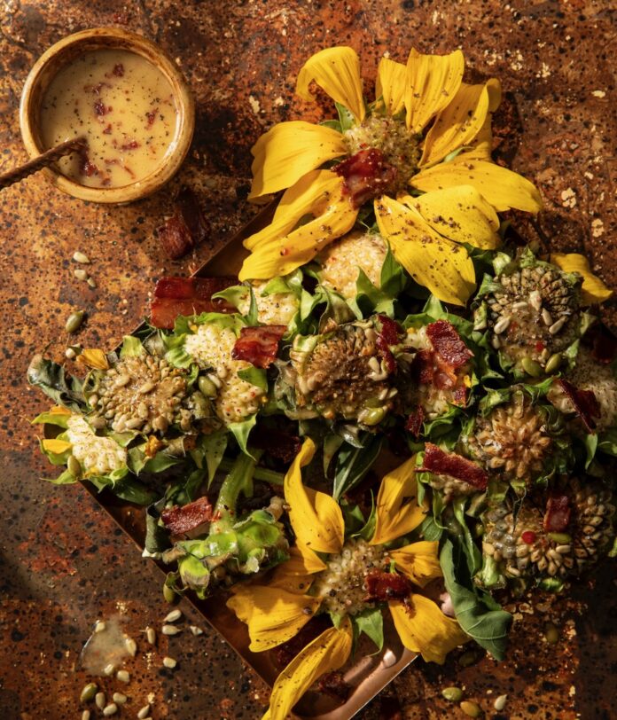 On a table sets various heads of grilled sunflowers with a bacon vinaigrette in a cup up in the top left corner.