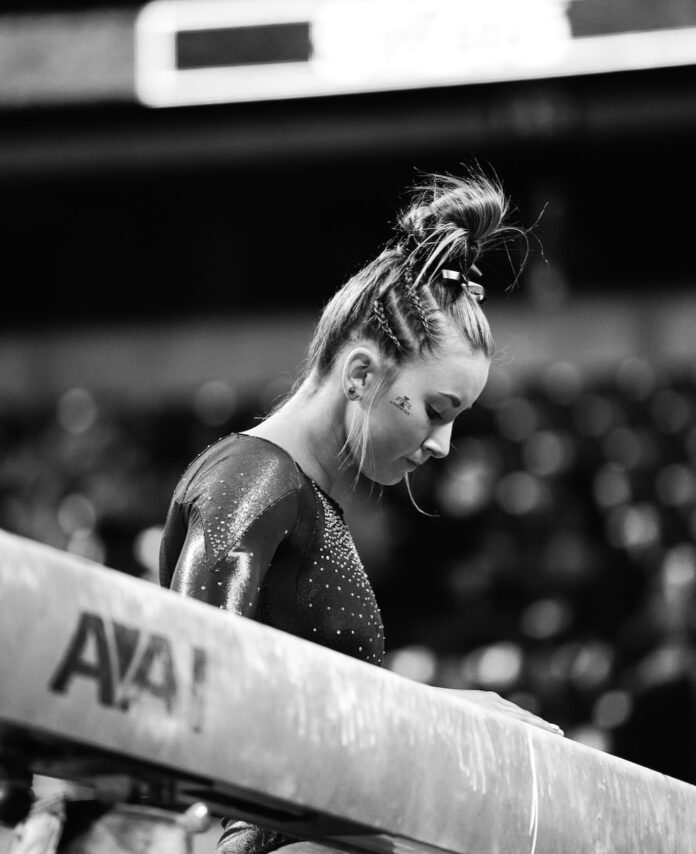 A woman looks down at a gymnastics balance beam colored in black and white.