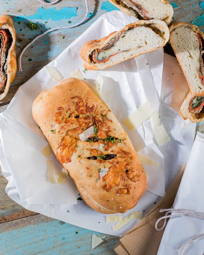 A pizza roll hot pocket lays on a piece of butcher paper as another lays split open, facing the camera in the upper right hand corner.