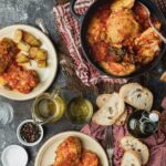 Various dishes on a dark grey countertop show chicken and potatoes in large groups.