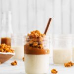 A small glass mason jar holds a popcorn panna cotta with a white creamy base, caramel, and carmael corn on top.