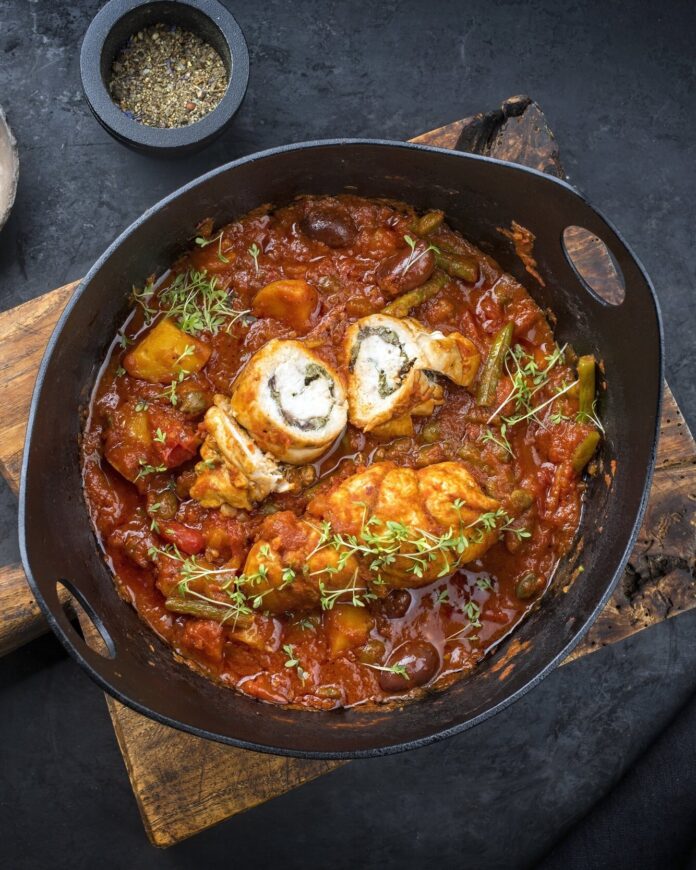 A pan holds a Sicilian Veal Roulade with plenty of herbs and a dark sauce on top.
