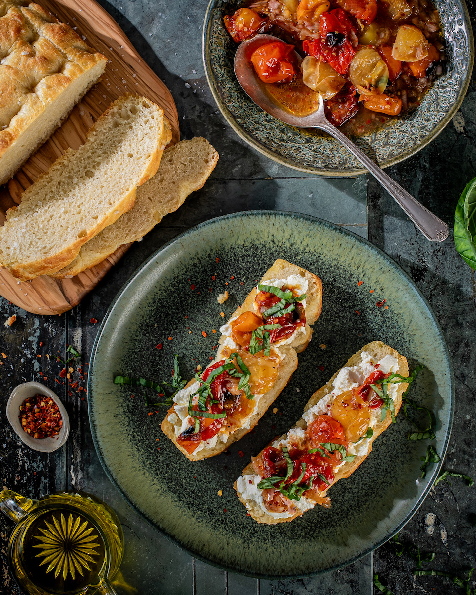 Charred tomato toast made in a woodfire oven with focaccia on a black background