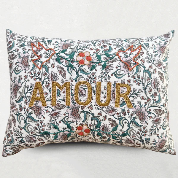 A pillow with plants on it and the word "amour" printed in gold 