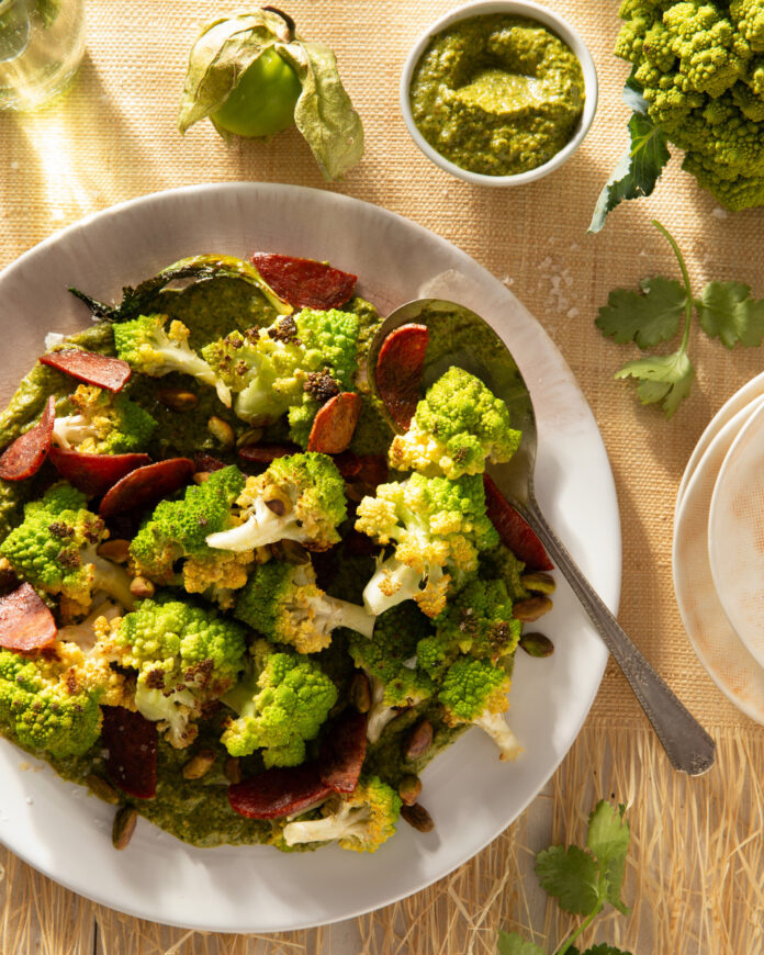 A plate of romanesco and chorizo on a tan table surrounded by spices