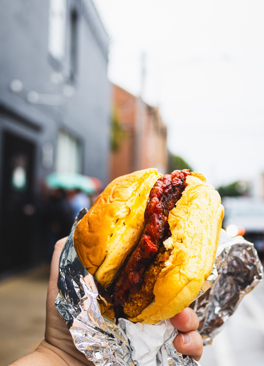 A breakfast sandwich featured in The Bear is held outside of a black restaurant featuring sausage, egg, and hashbrowns.
