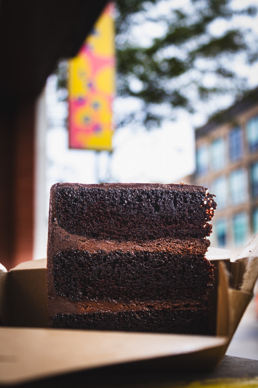 A piece of layered chocolate cake from The Bear sits in a box in front of Loaf Lounge. 
