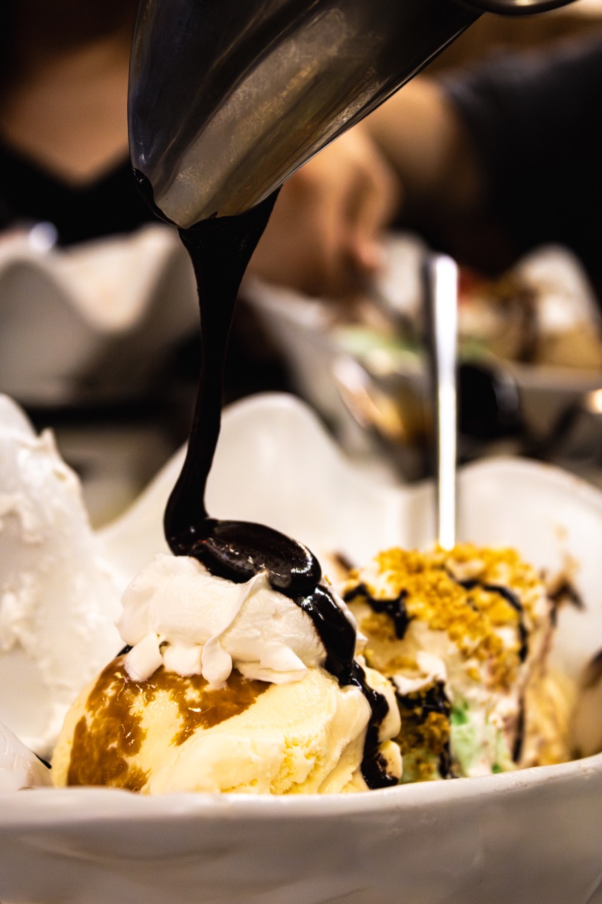 A person drizzles hot fudge onto an ice cream sundae. 