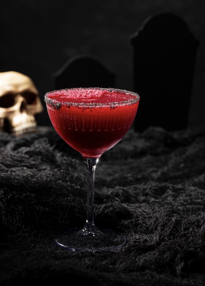 A blood beet red mocktail sits in a tall glass with black salt on the rim and a skull sitting in the background.