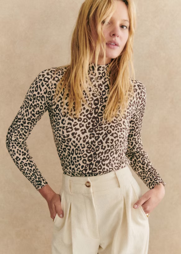 A blonde woman poses in a fall leopard print jumpsuit and white dress pants. 