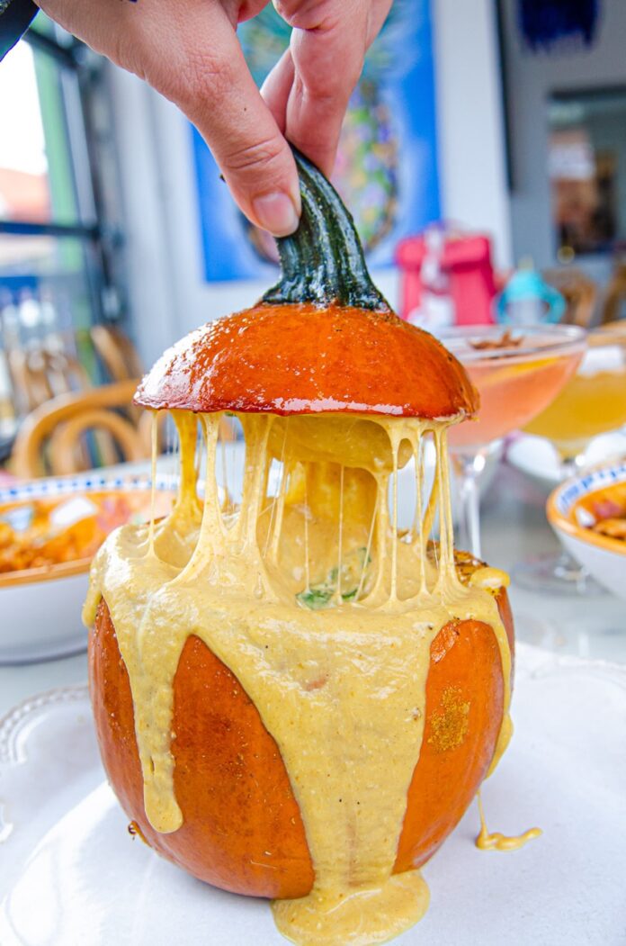 A person pulls off a lid of a pumpkin full of creamy cheese.