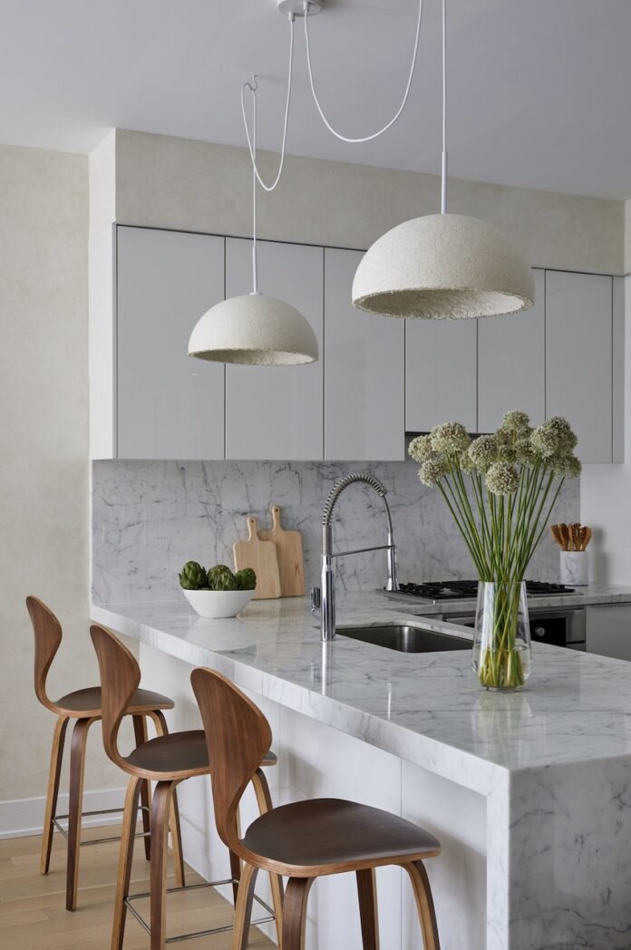 Two MushLume lamps from Parsons School of Design sit over a kitchen counter with a sink and chairs at it.