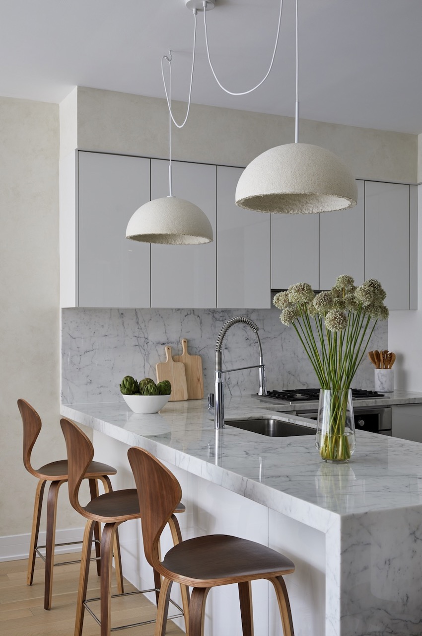 Two MushLume lamps from Parsons School of Design sit over a kitchen counter with a sink and chairs at it. 