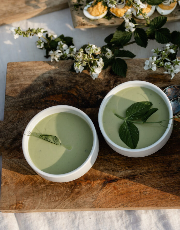 Pea Soup with Creme Fraîche and Mint Two green bowls of soup laid on a rustic cutting board and arranged with flowers.