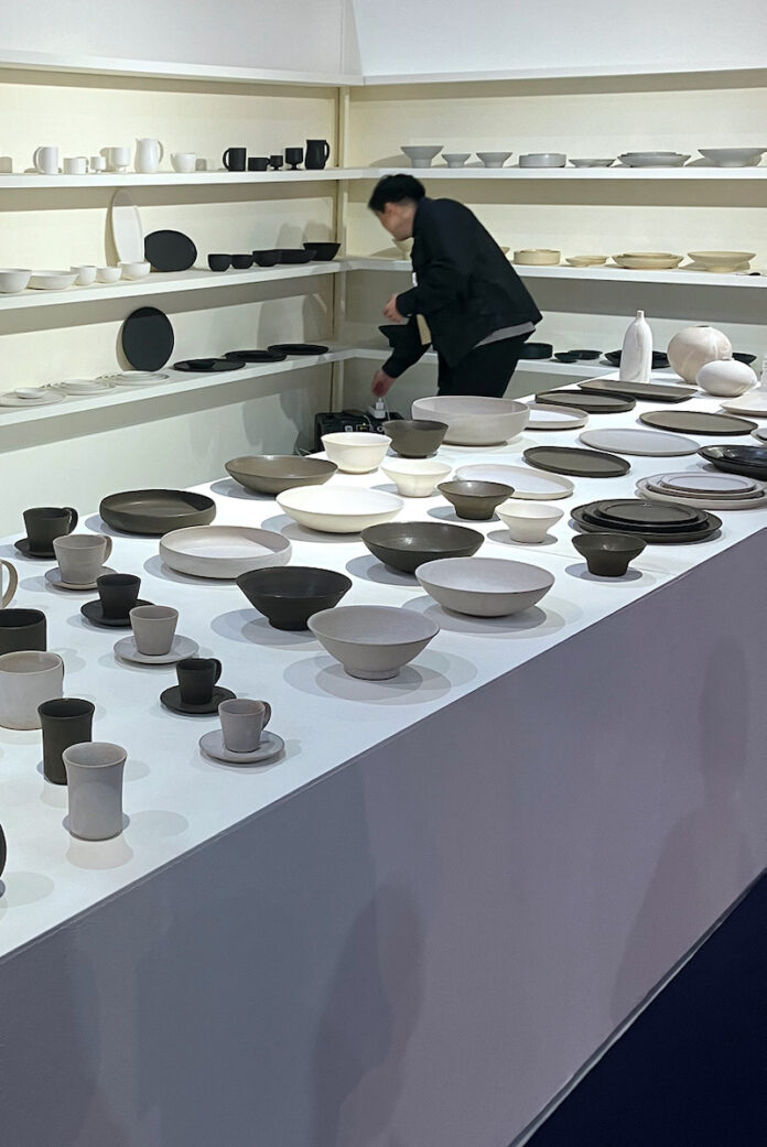 Black and white ceramics on a table, with a man in black stooping to look at them.
