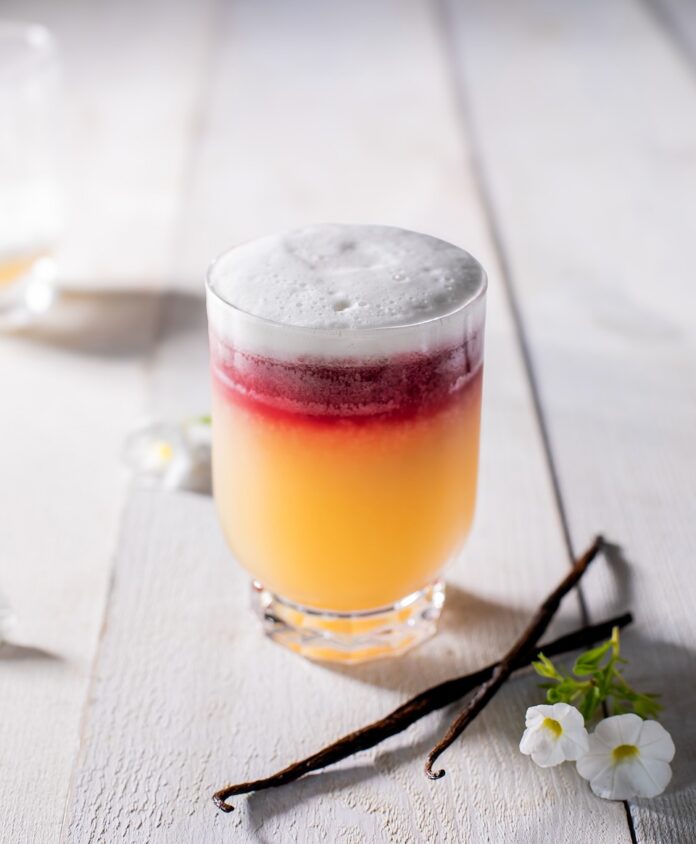 A short cocktail glass with a New York Sour in waves of orange, red, and white foam on top.