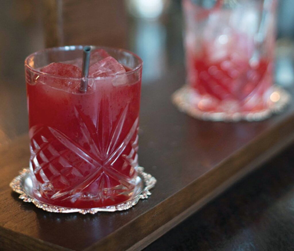 A red cocktail in a glass on a wood bar.