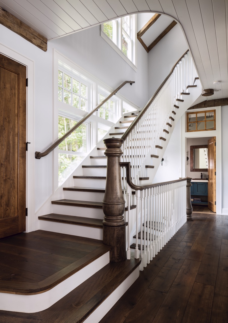 A white and wood staircase stretches upstairs. 