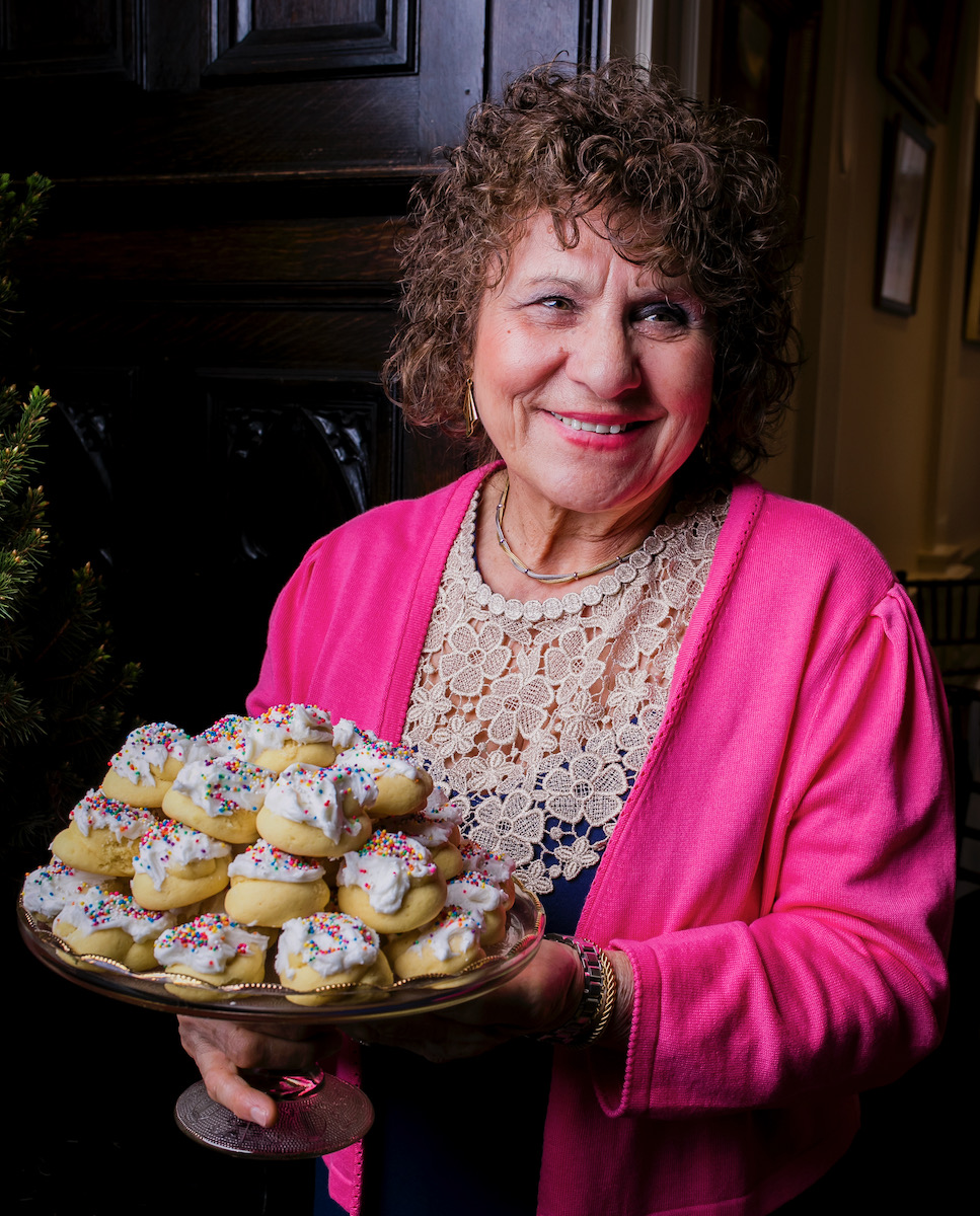 A woman in a pink jacket holds a tray of Italian wedding cookies 