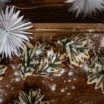 Rosemary shaped and decorated sugar cookies sit on a brown table sprinkled with powdered sugar.