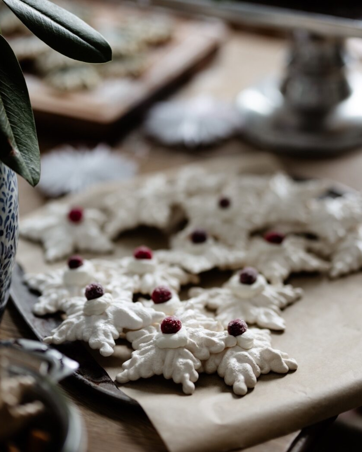 A plate full of French meringue cookies in snowflake shapes and topped with cherries amongst a table full of cookies.