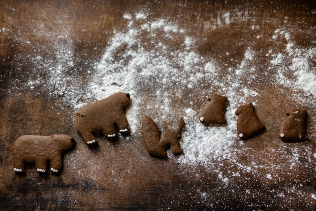 Animal shaped gingerbread cookies decorated with powdered sugar sit on a brown table coated in powdered sugar.
