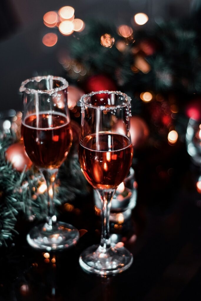 Two champagne flutes with red wine on a holiday table with lights and bulbs.