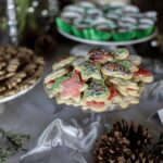 A glass platter full of Iced Sugar Cookies in star and snowman shapes and green and red colors amongst a table full of cookies.
