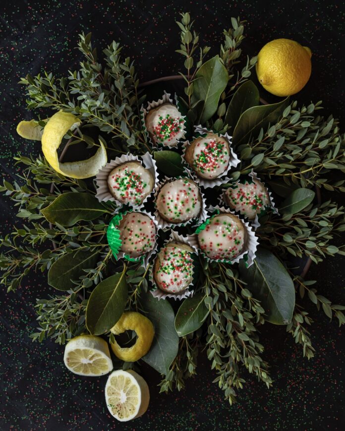 Italian Lemon Ricotta Cookies A small pile of Lemon Ricotta Cookies sit on leaves of greenery with lemon peels scattered throughout.